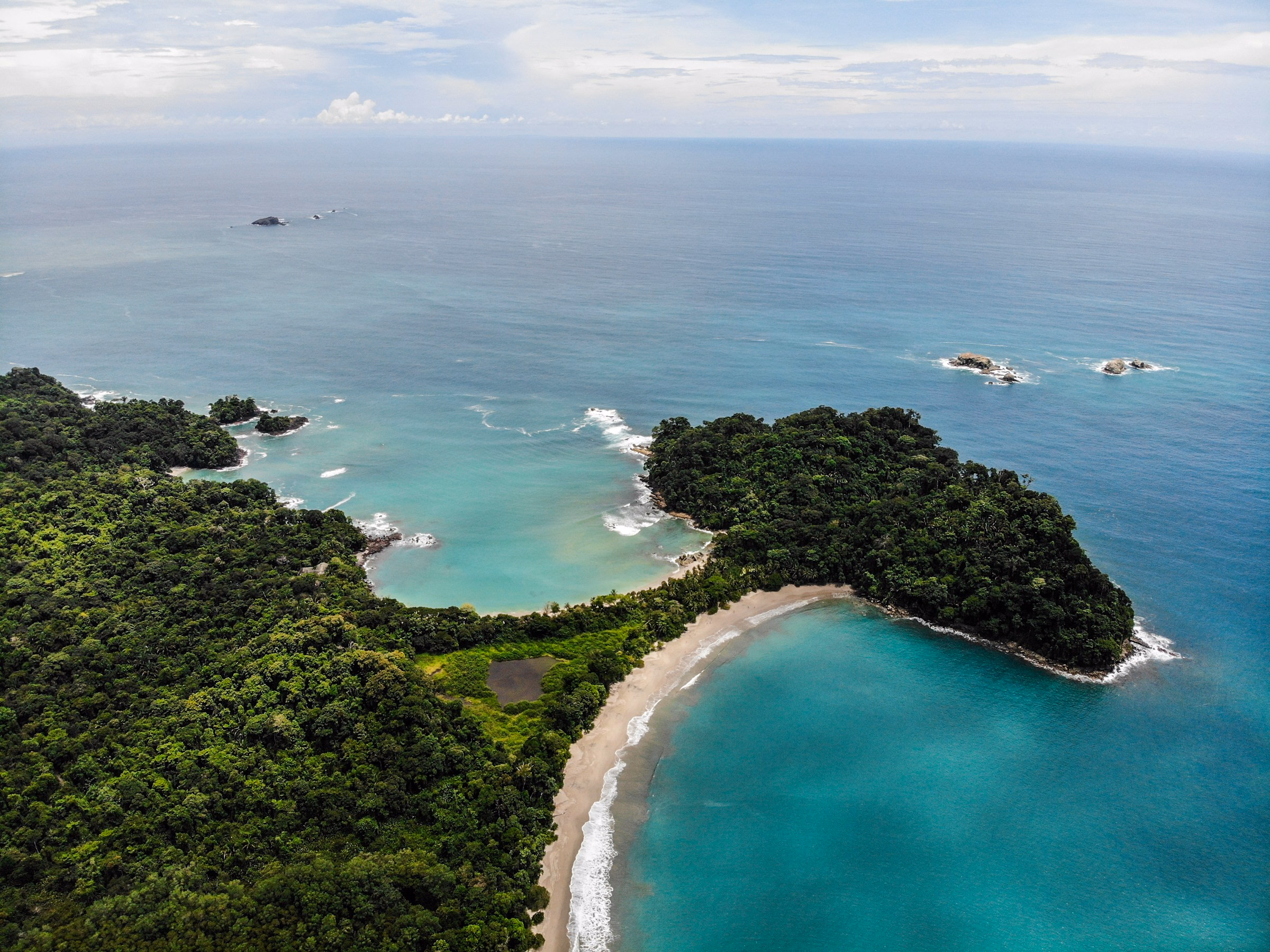 Aerial view of a rainforest headland meeting a curved beach and turquoise water on the Costa Rican coast