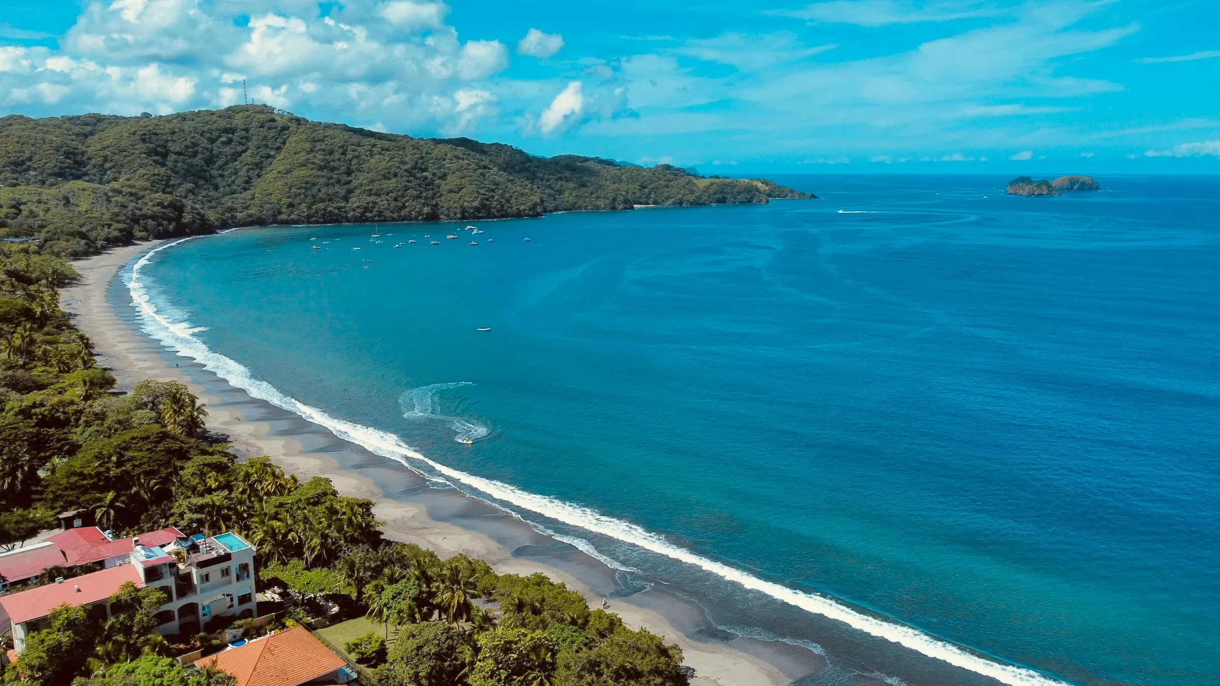Aerial view of a turquoise Guanacaste bay with a curving sand beach and houses among the trees